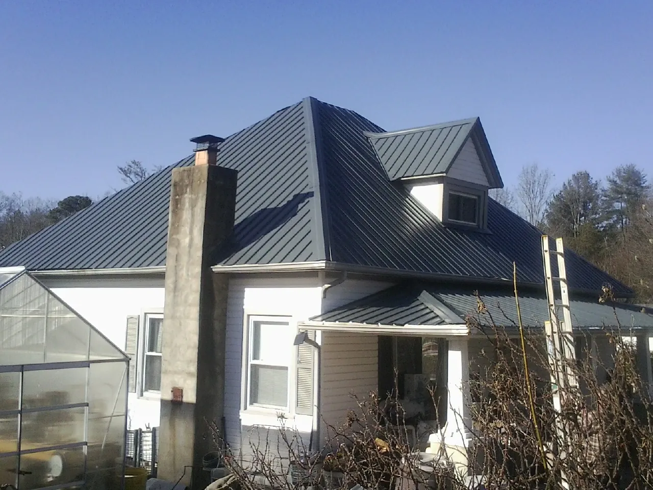 Dark blue standing seam metal roof on a white farmhouse with dormer — Slate & Tile Roof Repair by Roofing Brothers in Mulliken