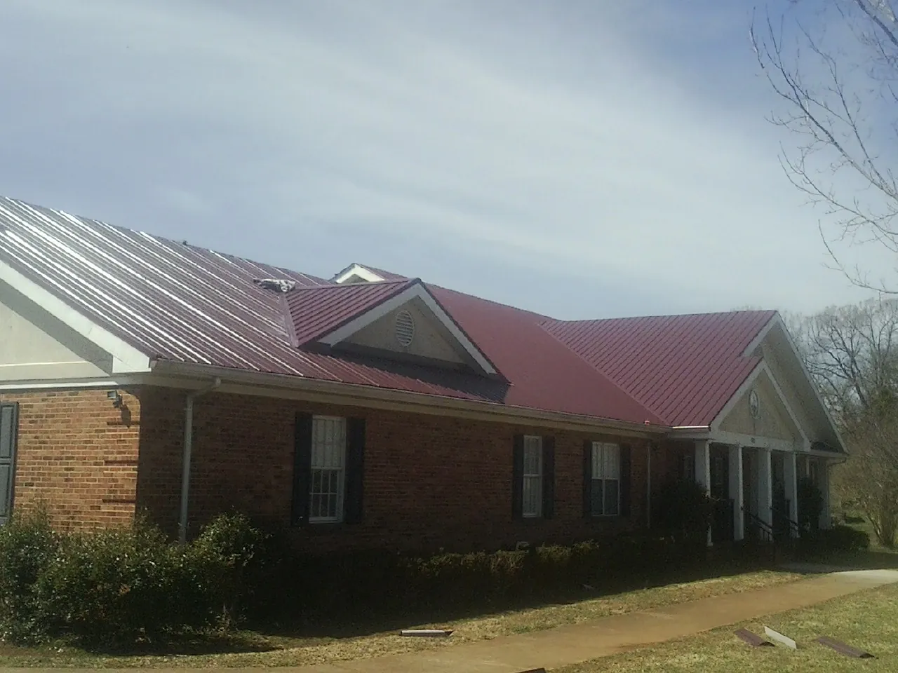 Red metal roof with gabled entries on a long brick building, from a Hail Damage Roof Repair job in Mulliken