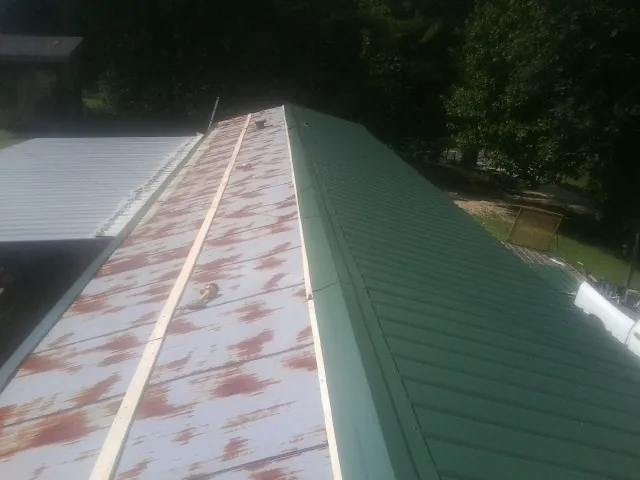 Old rusted panels beside newly installed green metal roofing — Wind Damage Roof Repair by Roofing Brothers in Mulliken