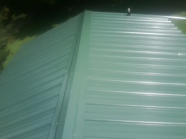 New green metal panels meeting at the ridge of a roof — Flat Roof Repair work by our crew in Mulliken