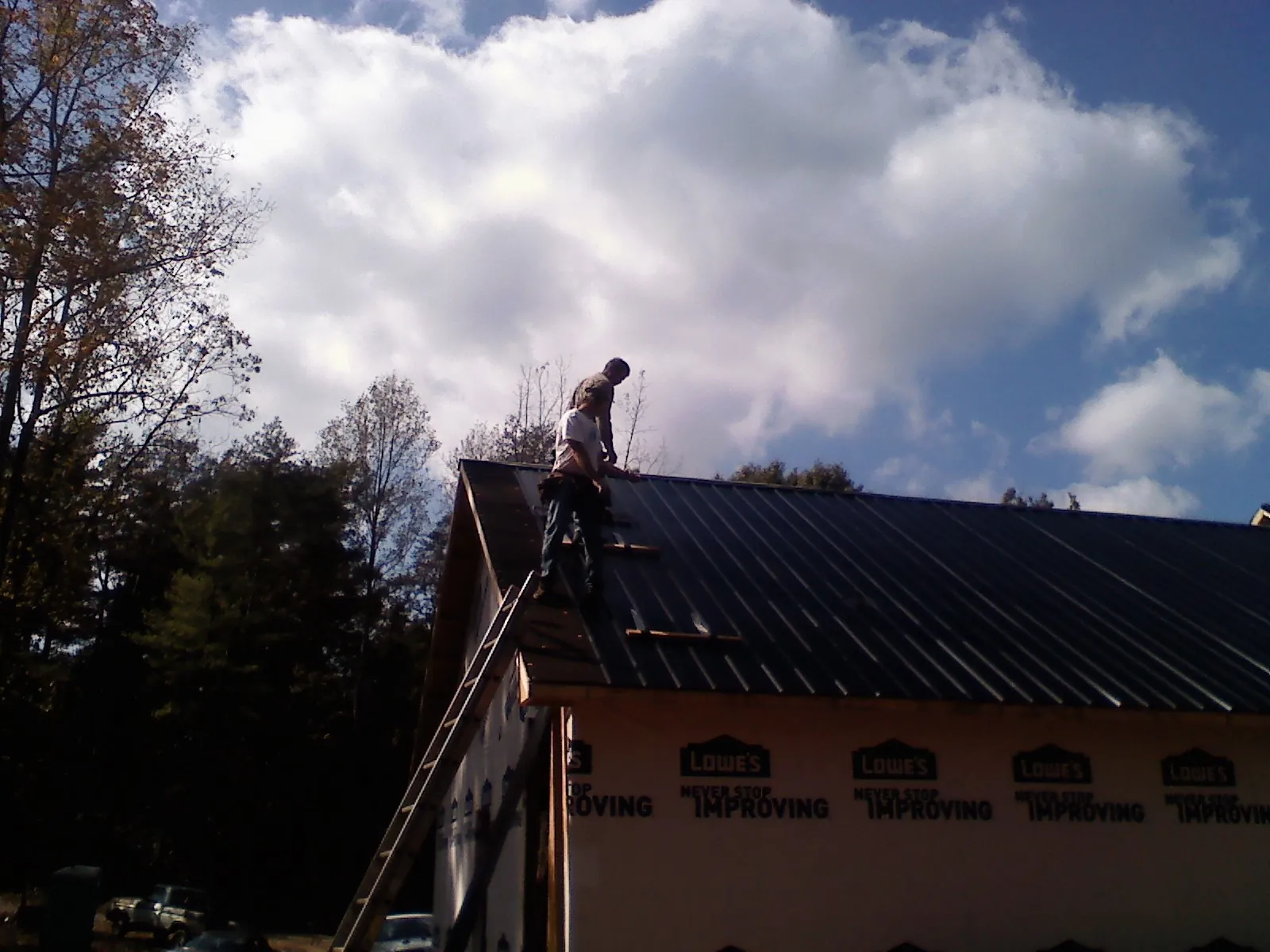Roofer fastening dark metal panels high against a cloudy sky, from a Roof Inspection job in Mulliken