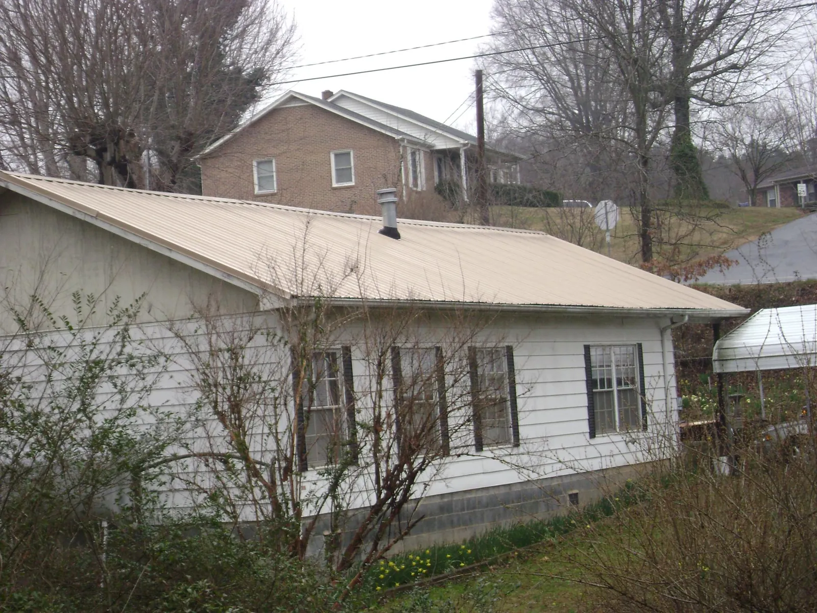 Tan metal roof on a white sided house set into a hillside — Commercial Roofing by Roofing Brothers in Mulliken