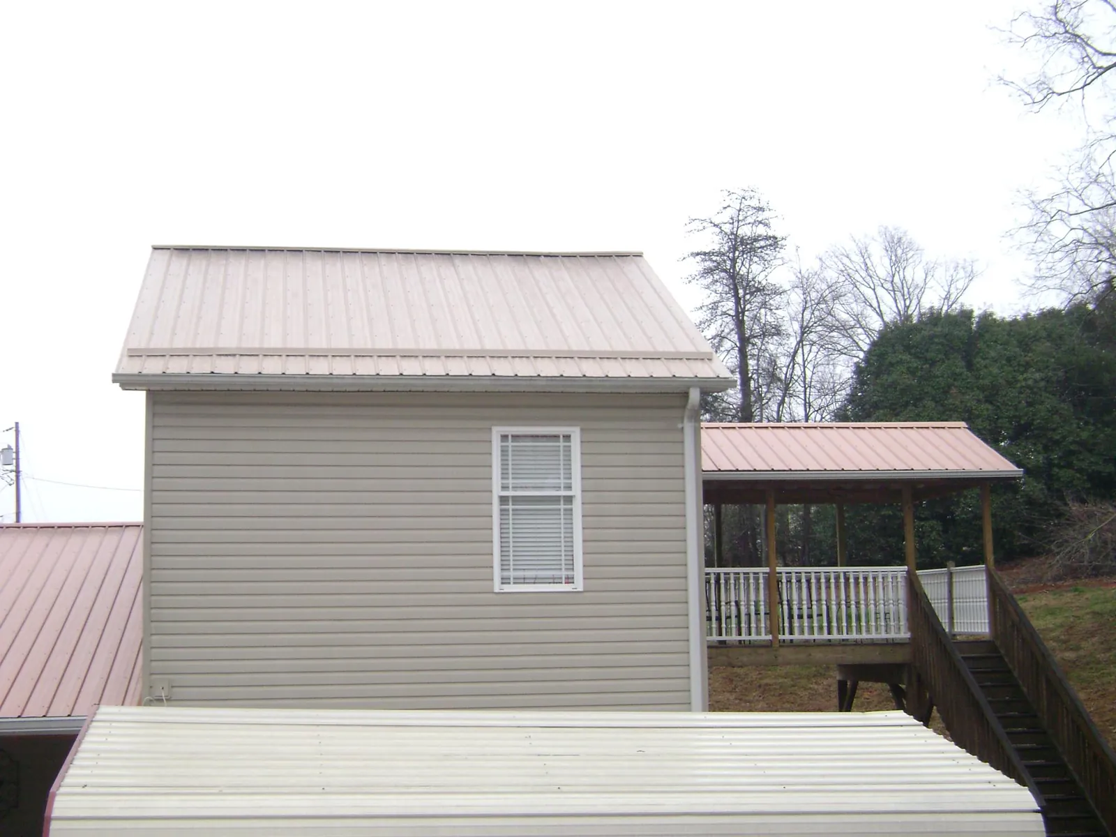 Tan metal roofs on a two story addition and attached porch, from a Roof Replacement job in Mulliken